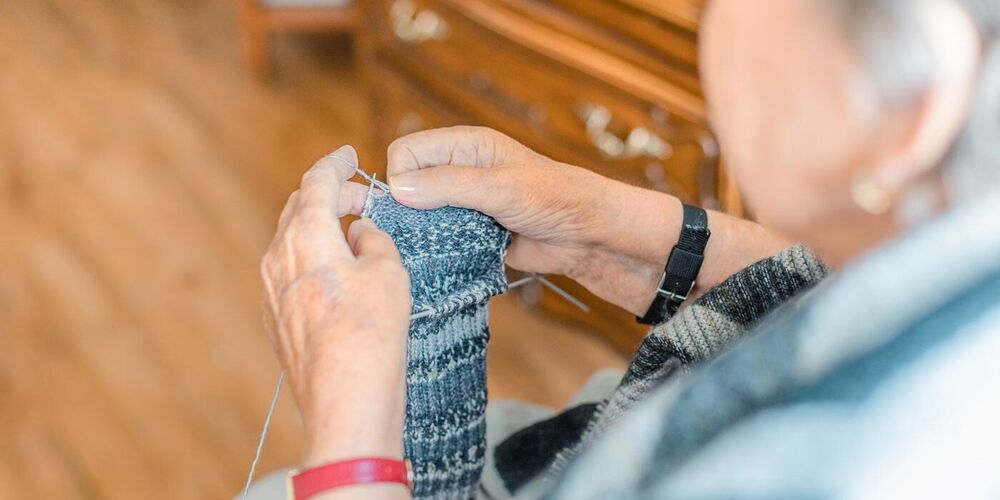 Eine Seniorin die Stricknadeln in der Hand hält und strickt. 
